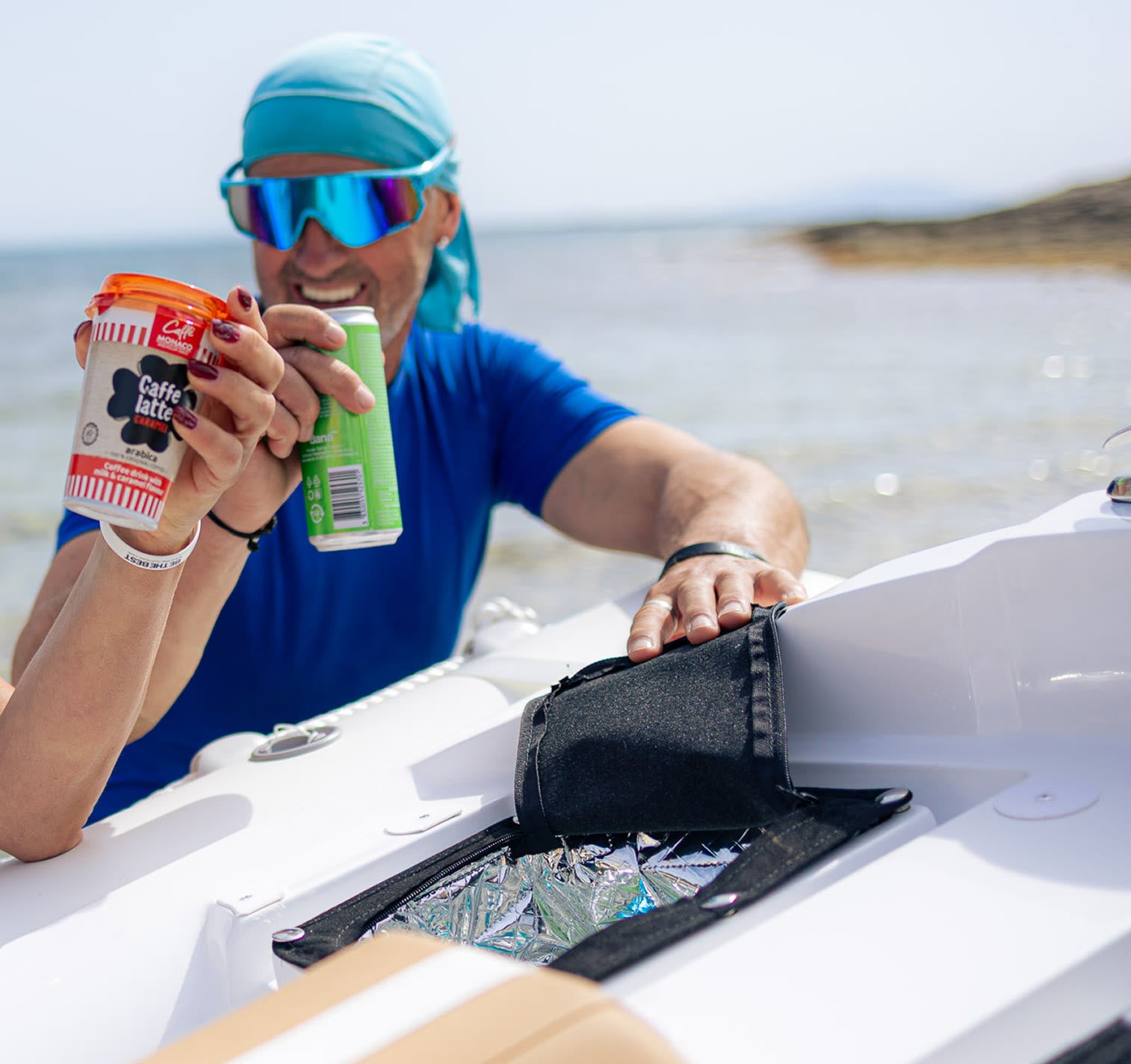 Person in a boat holding a can of Caffe Mio and a green bottle, with a scenic background.
