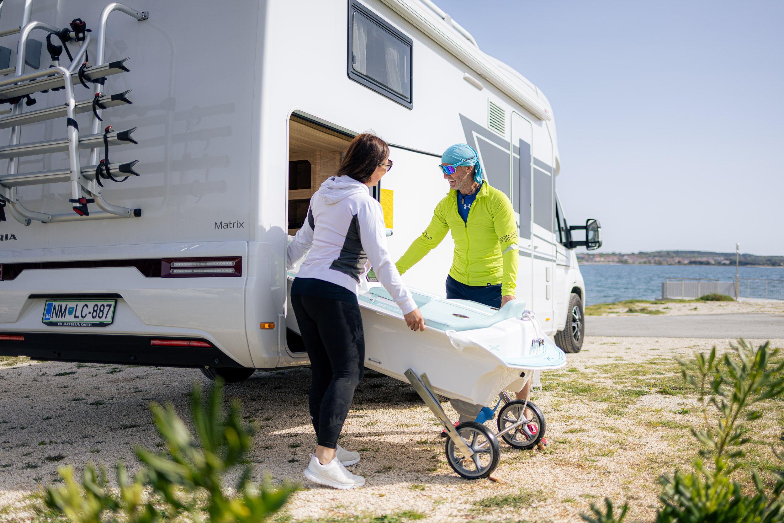 Two people with a camper van by a body of water